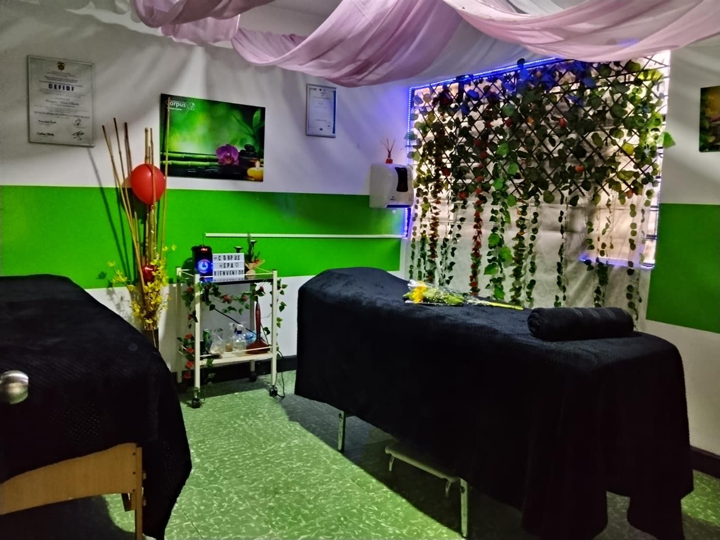 Cabina de Corpus Spa con dos camillas negras, pared de enredaderas con luz violeta y cortinas