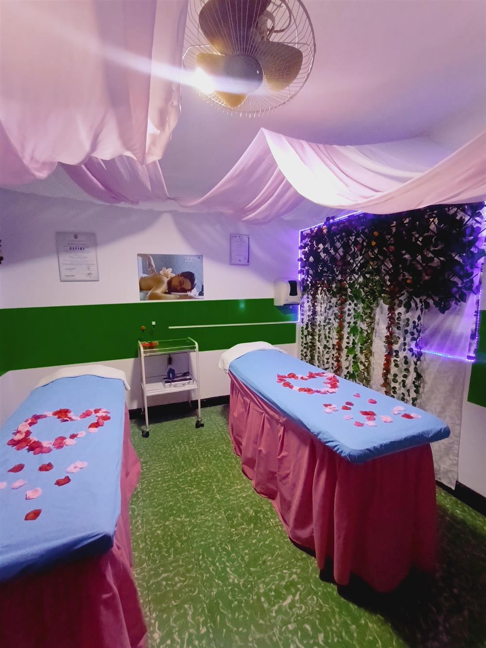Cabina de Corpus Spa con camillas, pétalos de rosa, cortinas rosadas y pared de enredaderas iluminada